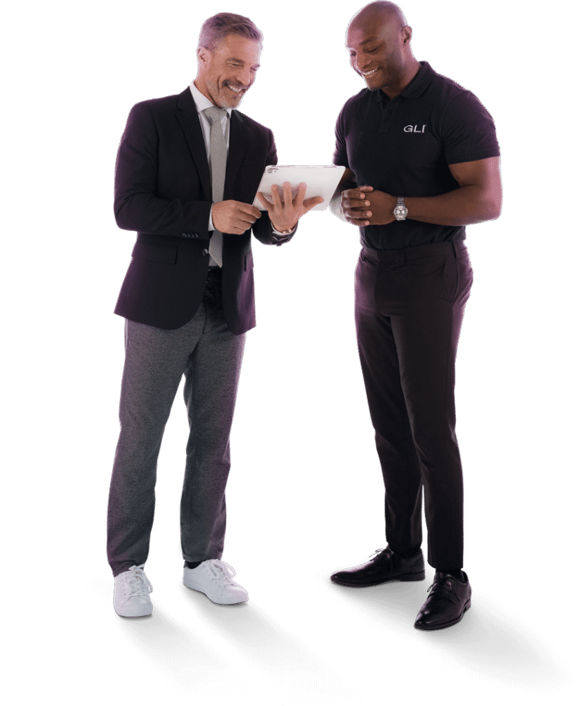 A man wearing a black polo shirt stands at a white adjustable desk working on a laptop with floating gaming-themed graphics.