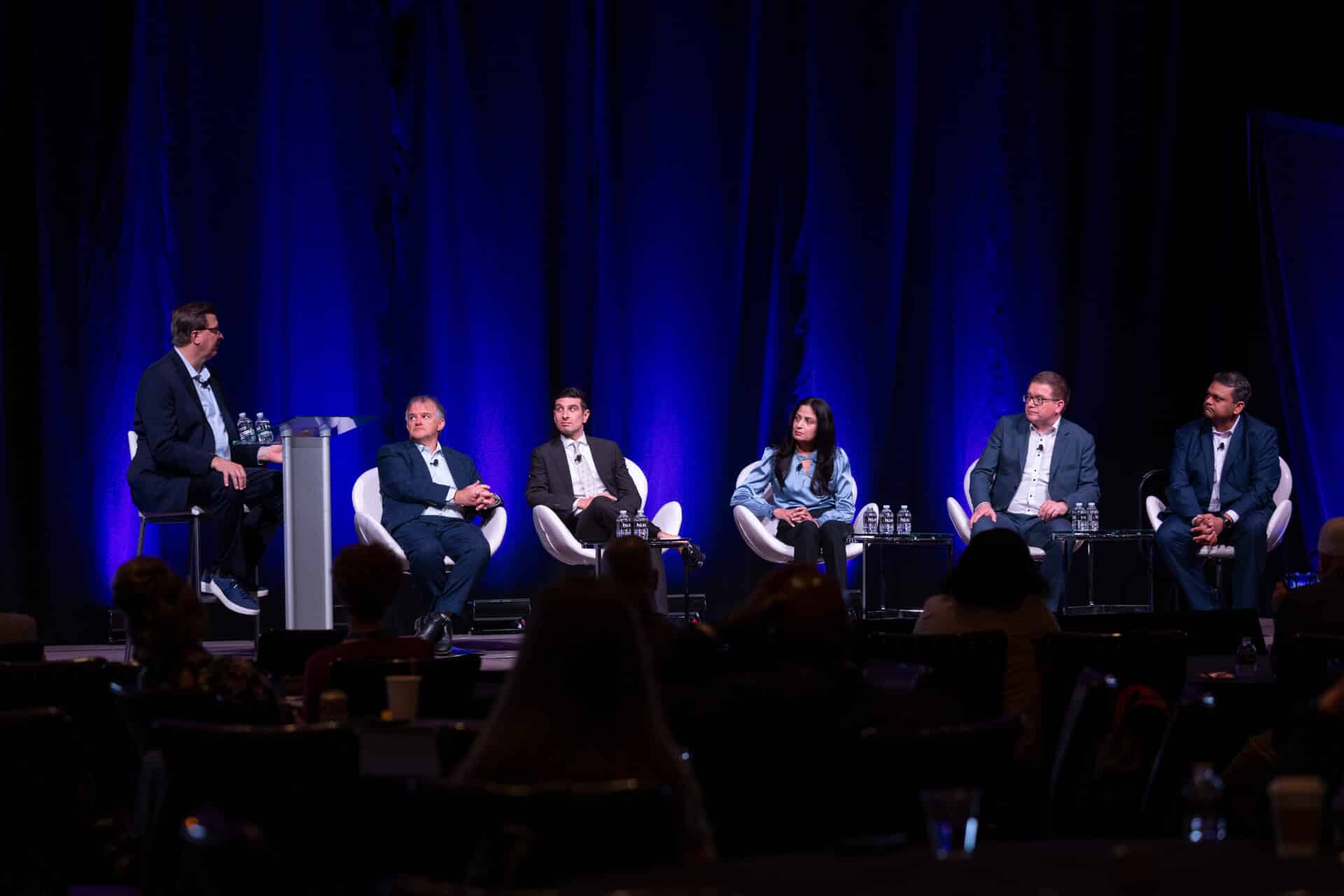 A wide view of five panelists seated on stage, taking questions from a moderator, at the Regulators Roundtable.